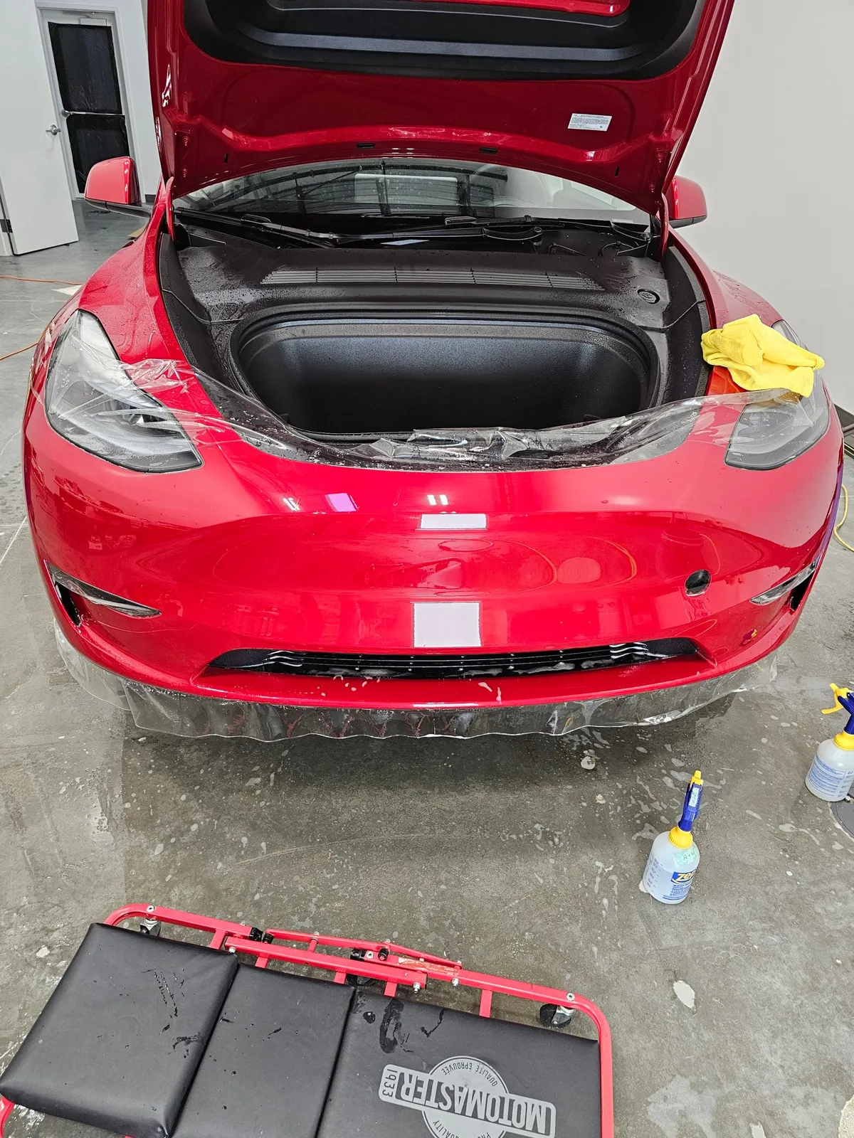 Red Tesla with the front bumper being wrapped in paint protection film.